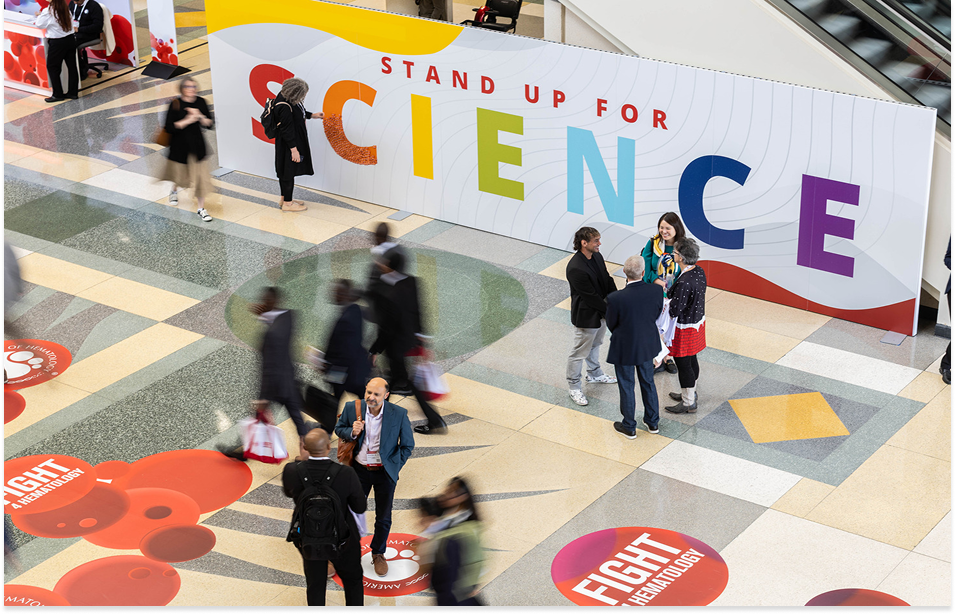 A photo of people walking at the ASH annual meeting with a bold poster of "stand up for Science"  on a side walk and Fight 4 hematology poster on the floor.